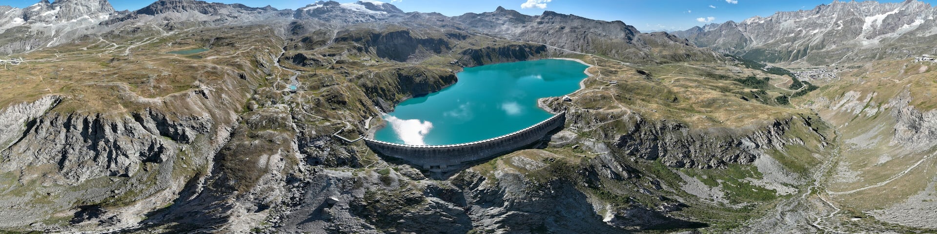 Aerial view of the Matterhorn, seen from Breuil-Cervinia. Green valleys and waterways flowing from the glaciers. Goillet reservoir and dam
