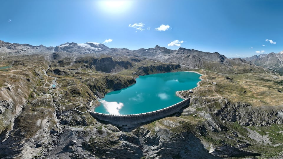 A mountain landscape with a large turquoise lake and a dam.