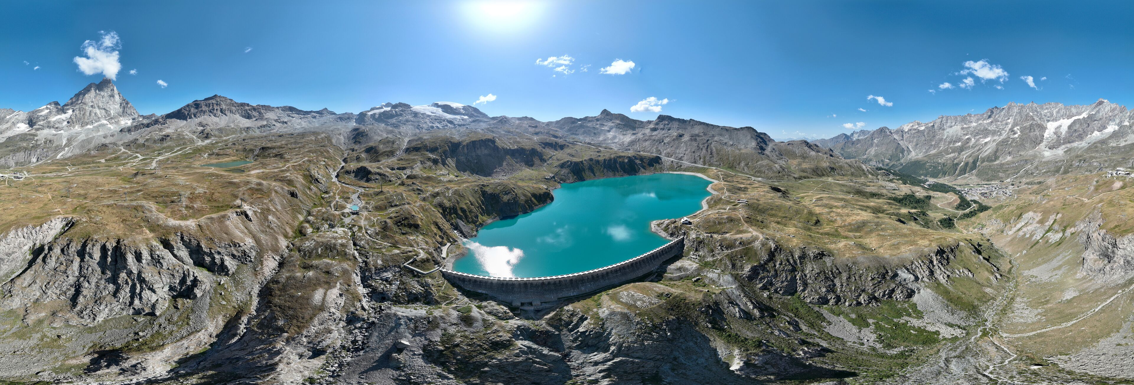 A mountain landscape with a large turquoise lake and a dam.