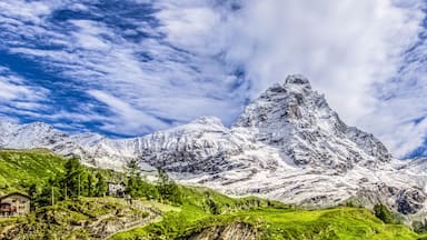 Un pico nevado de montaña con un chalet en primer plano y un cielo azul despejado.