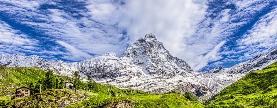 Panoramic view of the south face of the Matterhorn, view from the Breuil-Cervinia village.Green meadow in the front and blue sky with white clouds above mountains..Summer in the Alps, Italy, Europe.
