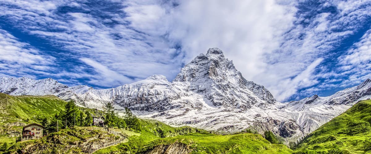 Panoramic view of the south face of the Matterhorn, view from the Breuil-Cervinia village.Green meadow in the front and blue sky with white clouds above mountains..Summer in the Alps, Italy, Europe.
