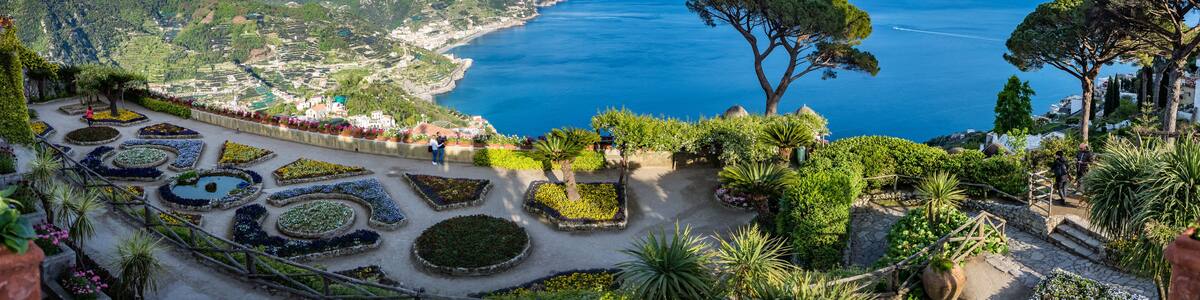Un paysage côtier avec des jardins en terrasses, un arbre remarquable et une vue sur la mer et les montagnes.