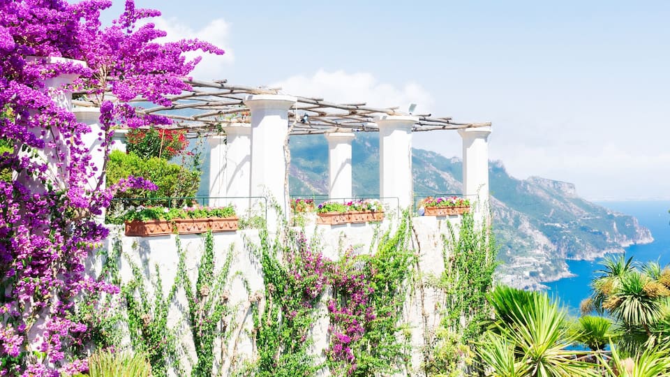 A white building with purple flowers and a view of the sea.