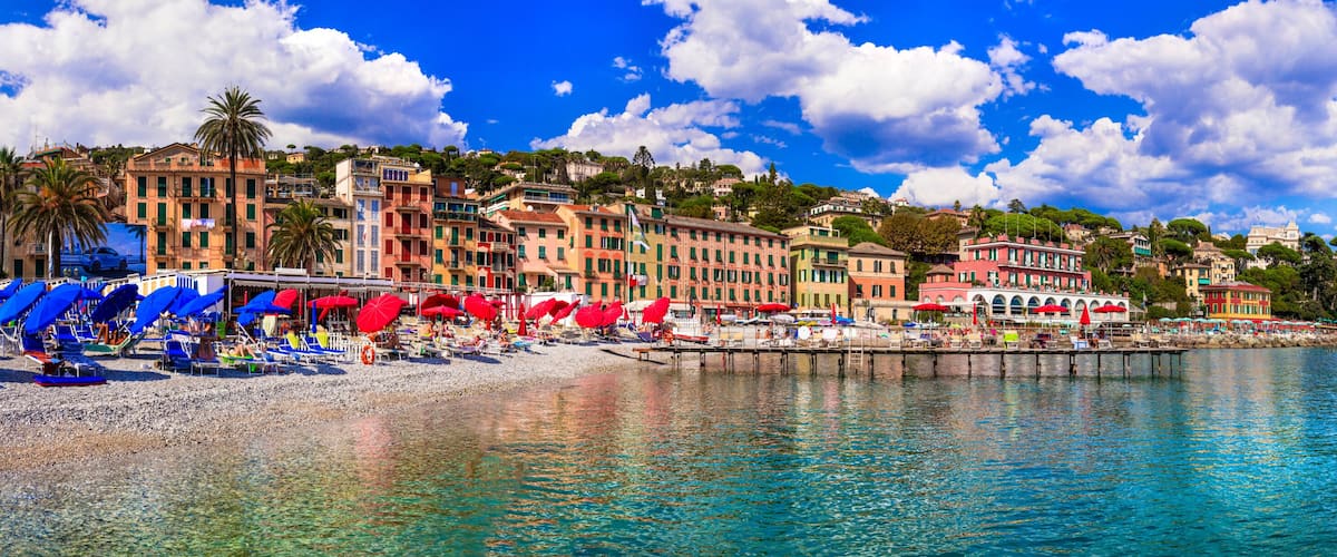 A coastal town with colorful buildings, a pebble beach, and clear blue waters.
