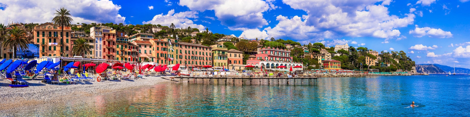 A coastal town with colorful buildings, a pebble beach, and clear blue waters.