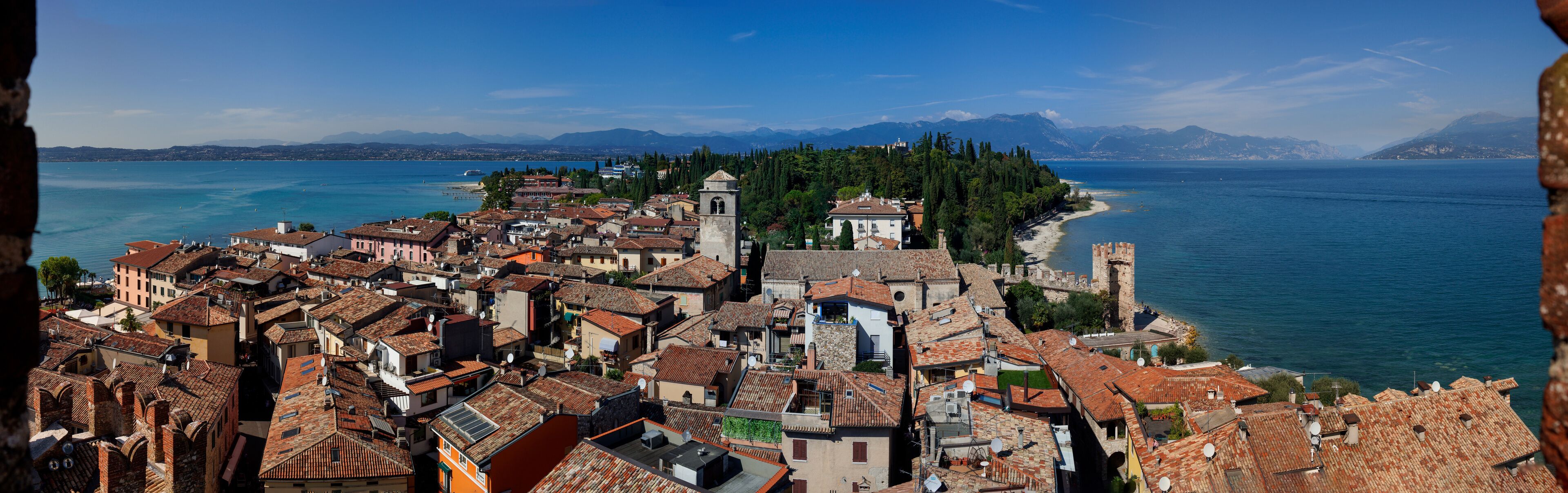 A coastal town with terracotta-roofed buildings, a prominent church tower, and a historic castle overlooking the sea.