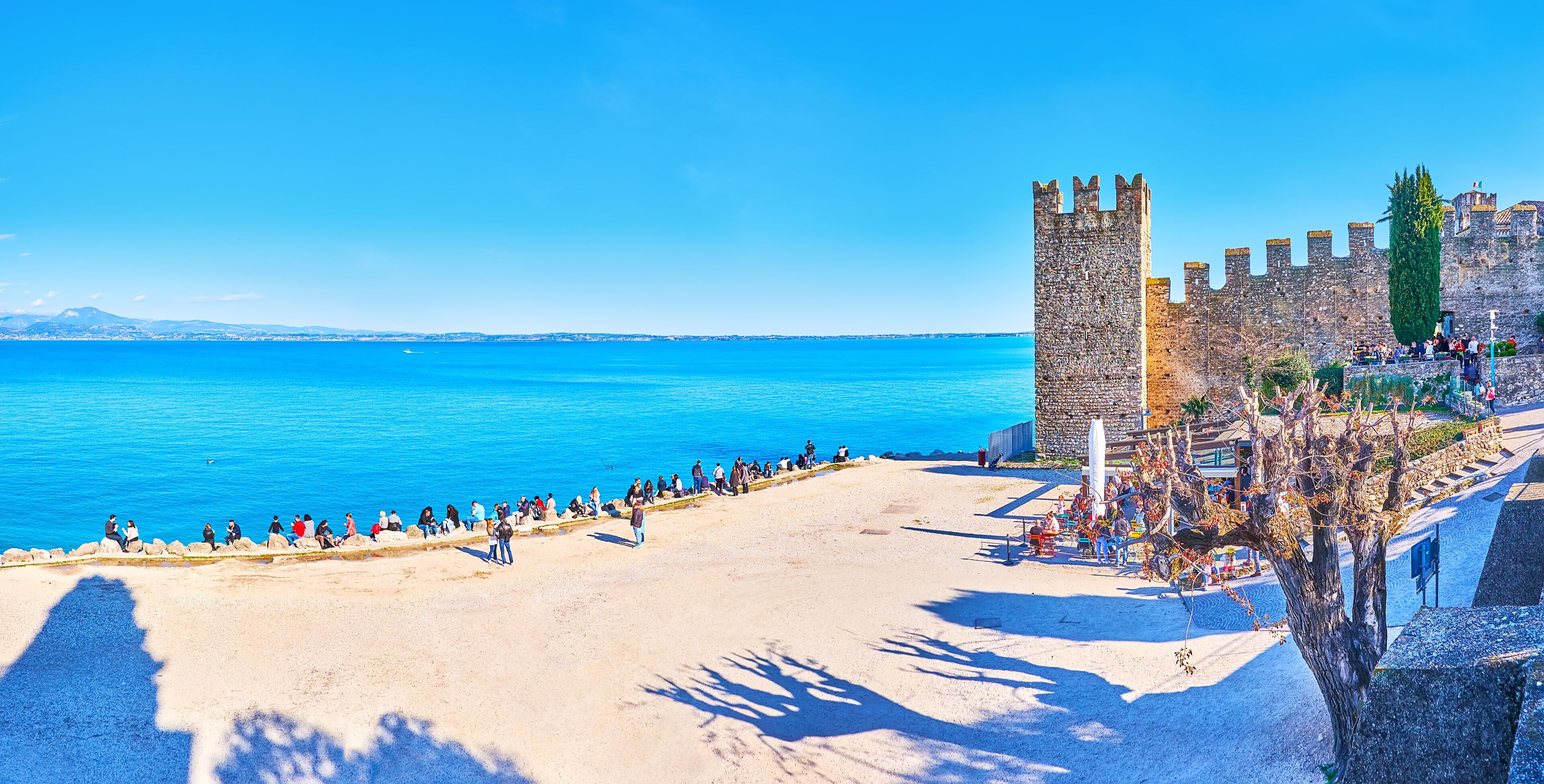 Una playa costera con una torre de piedra histórica y un mar azul transparente.