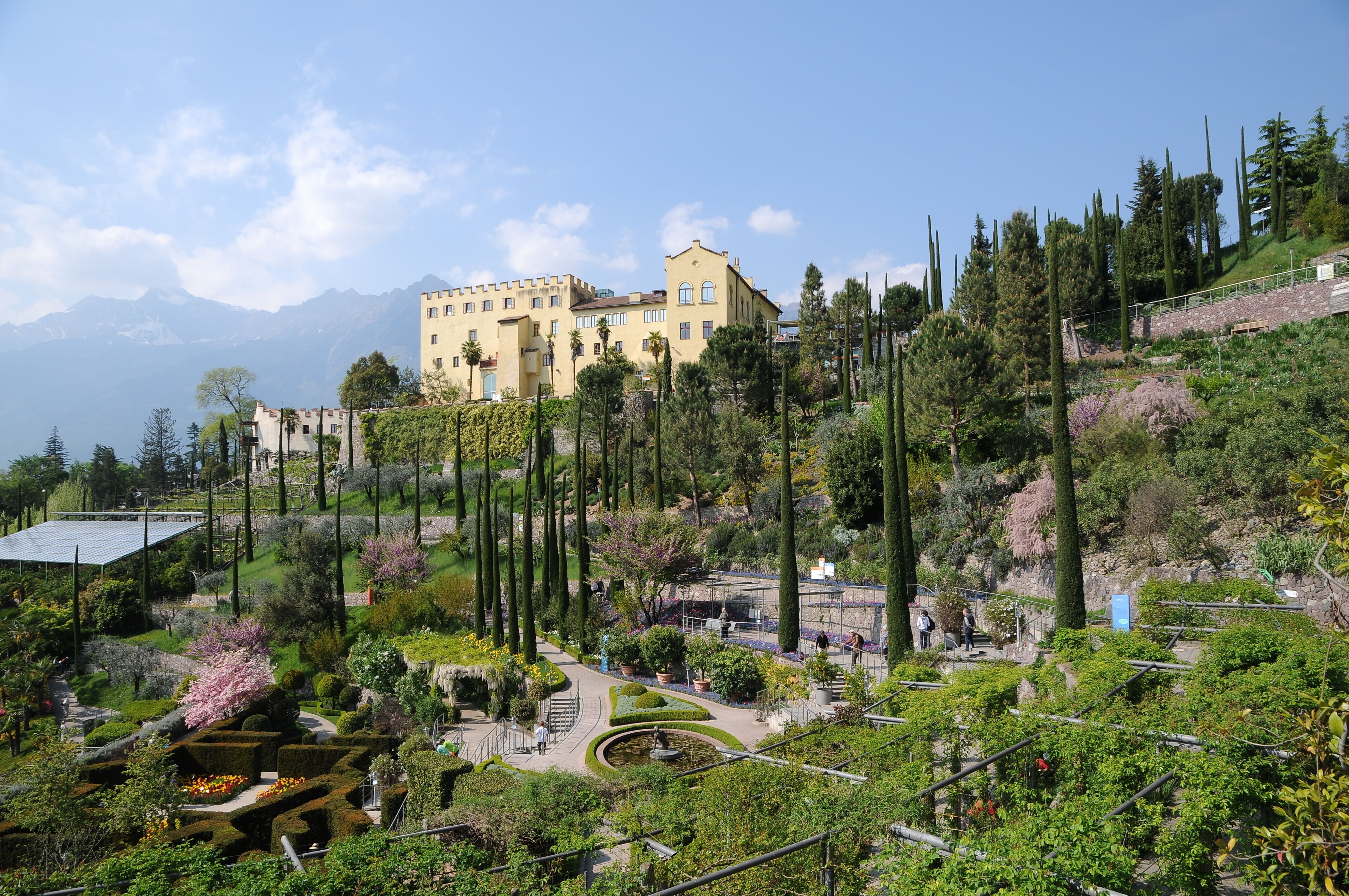 A castle on a hill with a garden and a mountain in the background.