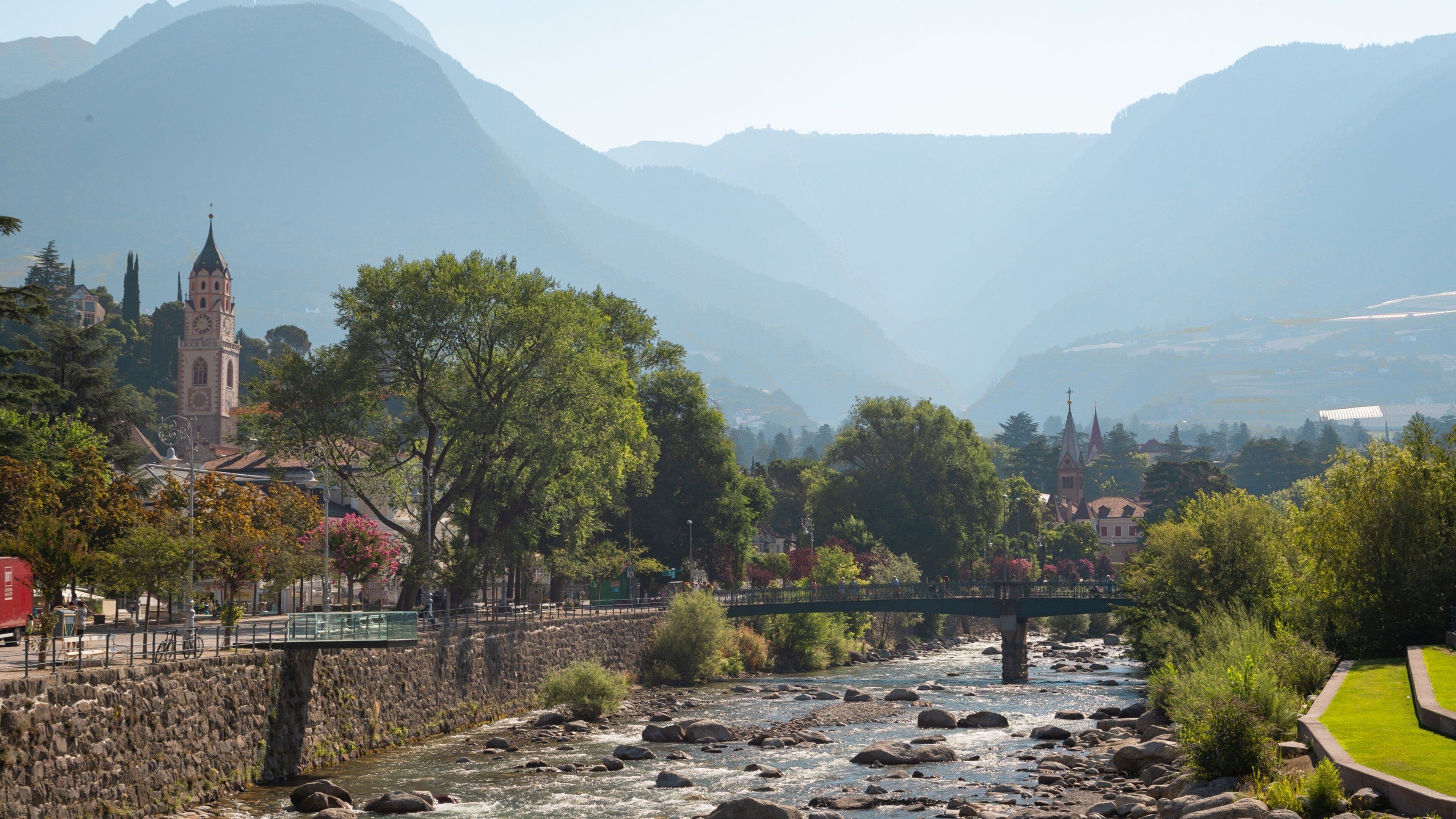 A river with rocks, a bridge, trees, and mountains in the background.