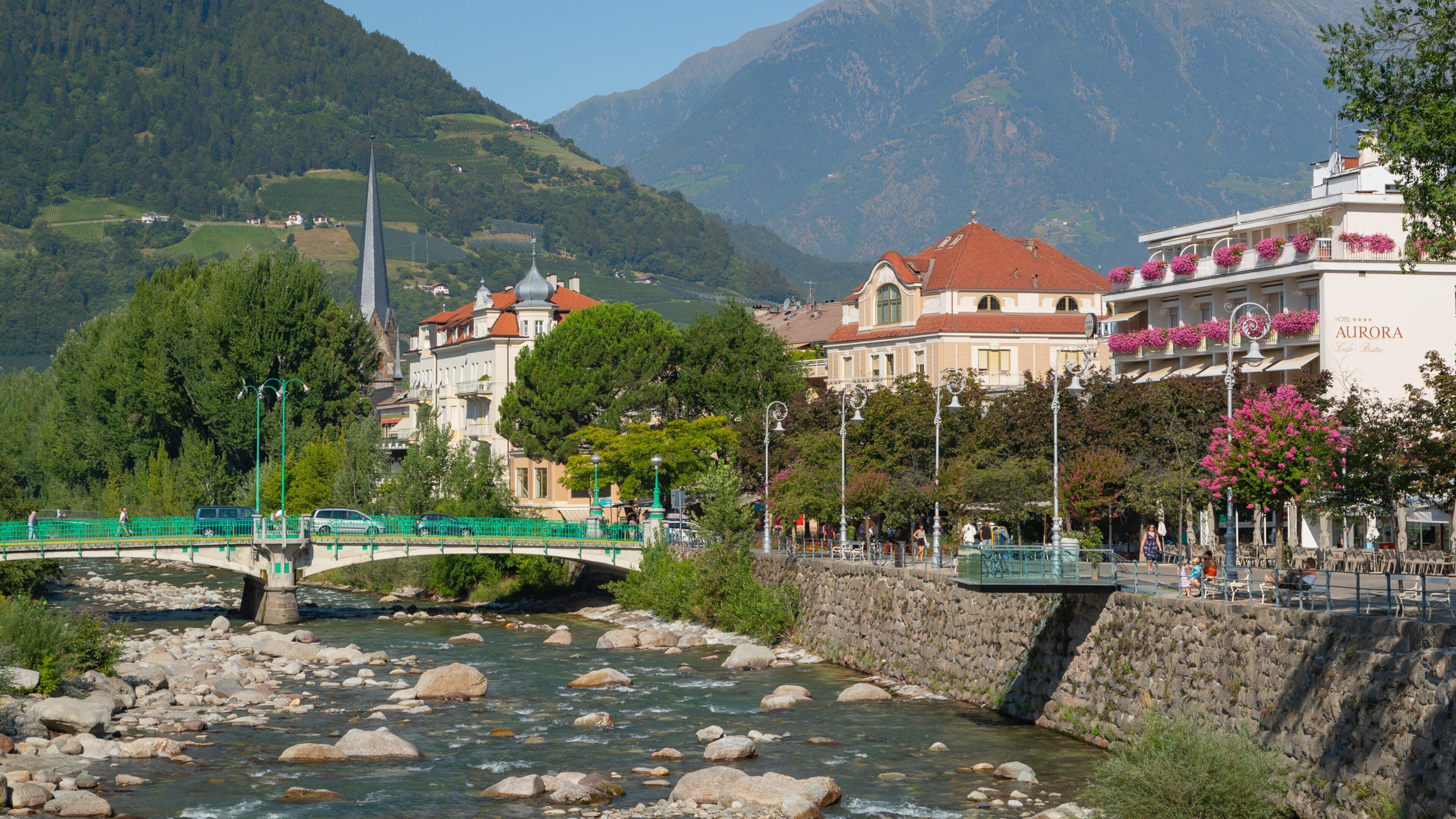 A river with rocks, a bridge, buildings, and mountains in the background.