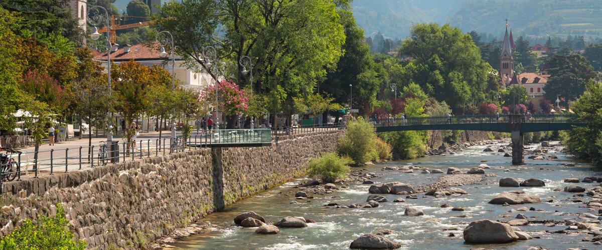 Un río con rocas, un muro de piedra, un puente y edificios al fondo.