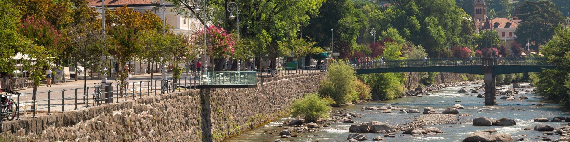 A river with rocks, a stone wall, a bridge, and buildings in the background.