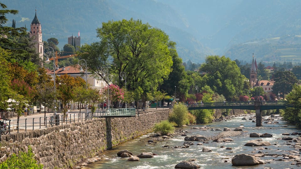 A river with rocks, a stone wall, a bridge, and buildings in the background.