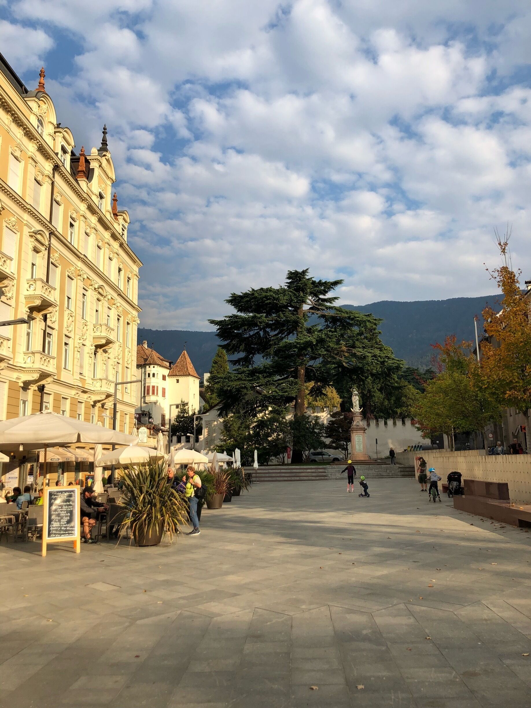 A square with a large tree, a fountain, and a building with ornate architecture.