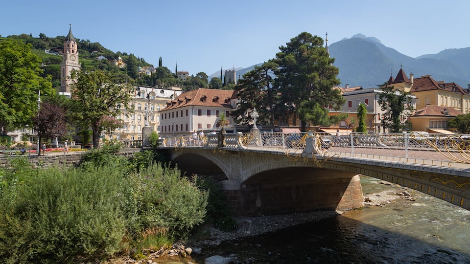 A stone bridge over a river, surrounded by lush greenery and historic buildings.