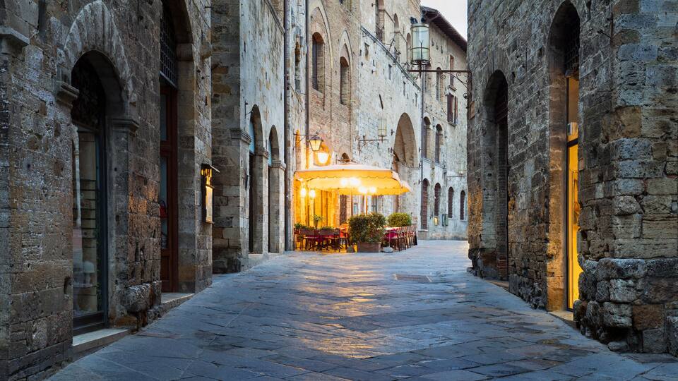 A narrow cobblestone street flanked by historic stone buildings with arched doorways and windows.