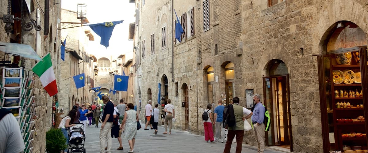 A narrow street with stone buildings, Italian flags, and a shop with ceramic plates.