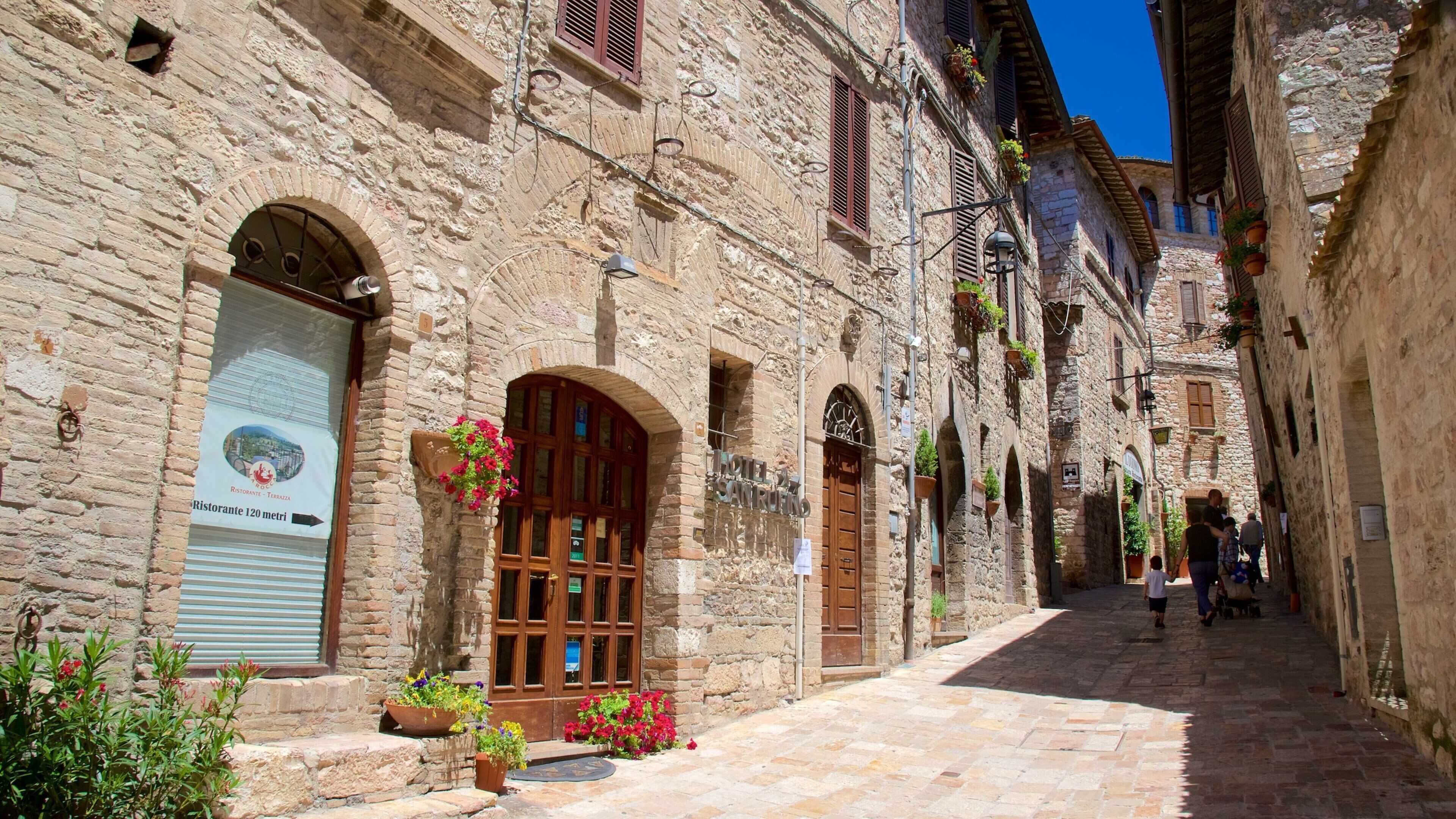 Una estrecha calle empedrada con edificios tradicionales, un letrero de restaurante y macetas colgantes de flores.