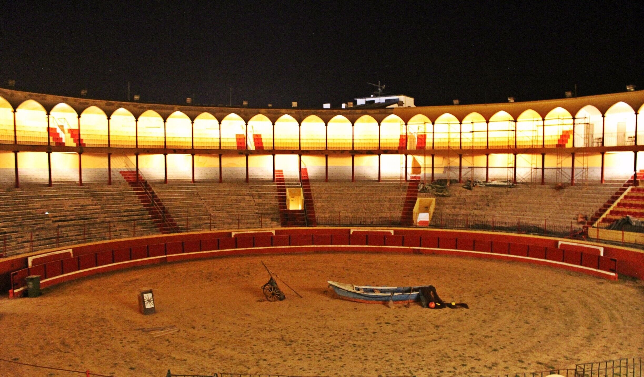 An empty outdoor amphitheater at night with tiered seating and a sandy stage area.