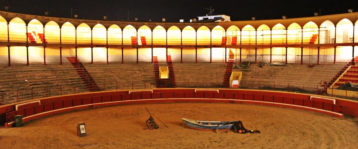 An empty outdoor amphitheater at night with tiered seating and a sandy stage area.