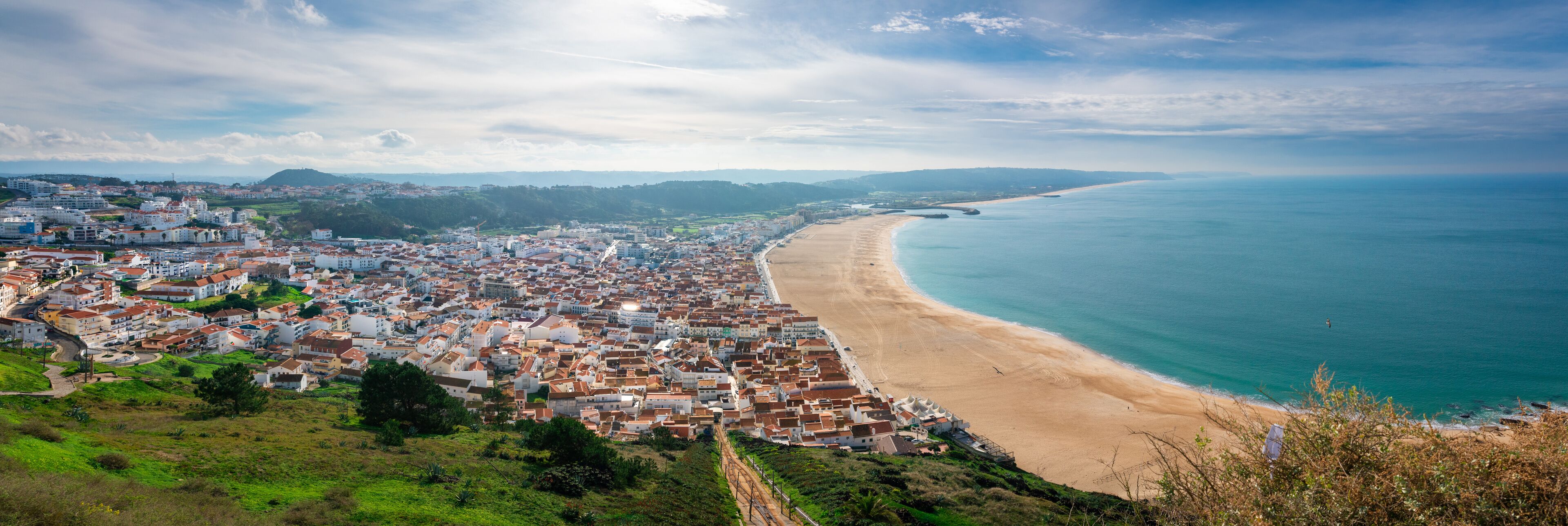 A coastal town with a beach, buildings, and a hilly landscape.