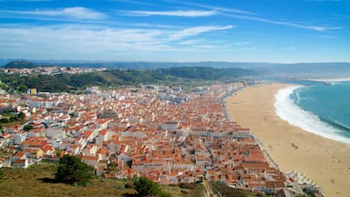 Uma cidade costeira com edifícios de telhados vermelhos, uma praia de areia e um céu azul claro.