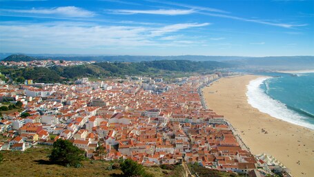 A coastal city with red-roofed buildings, a sandy beach, and a clear blue sky.
