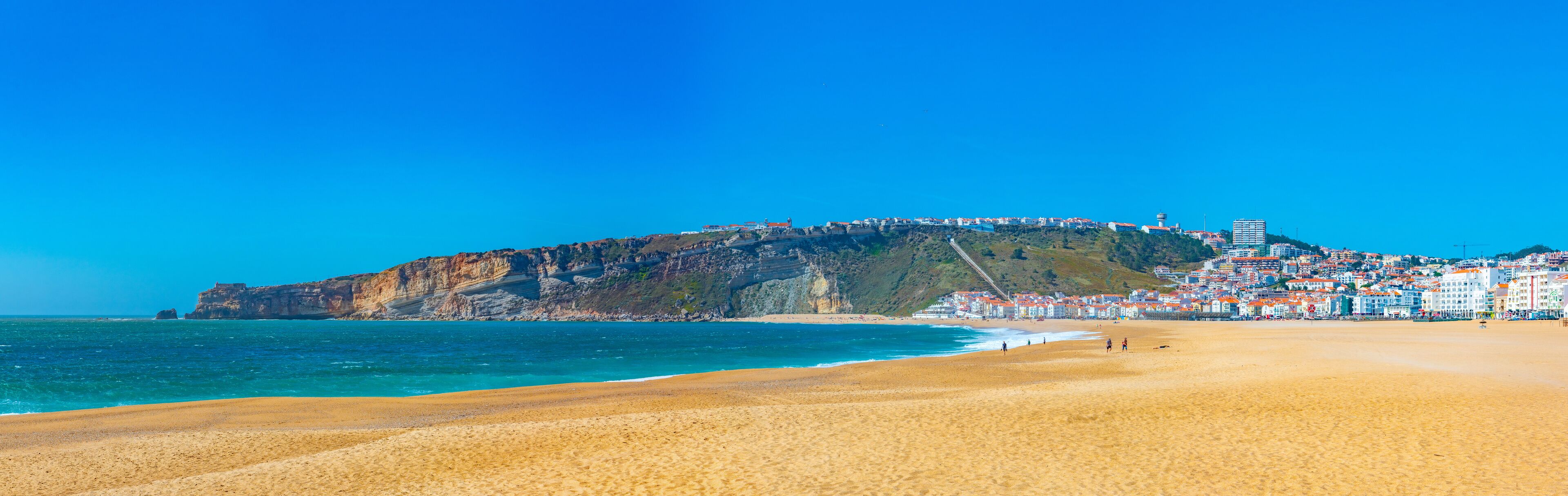 A coastal town with a prominent hill, beach, and buildings along the shore.