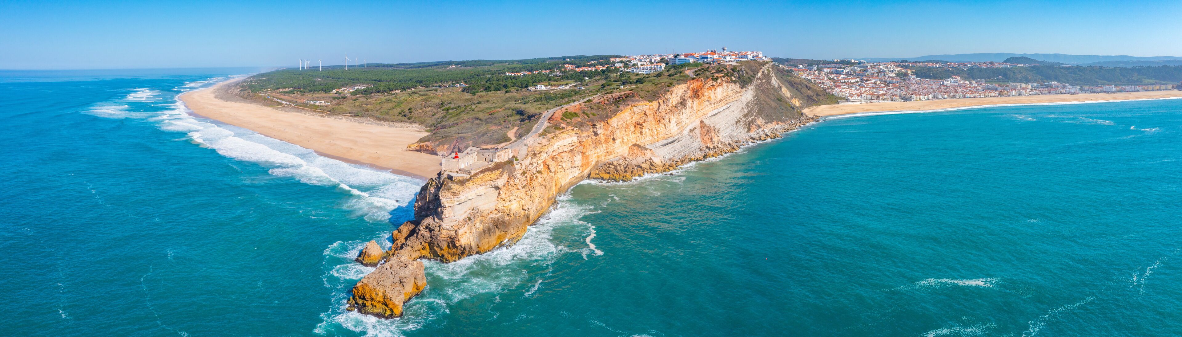 A coastal landscape with a cliff, beach, and wind turbines.