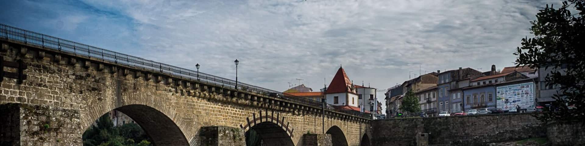 A stone bridge over a flowing river with a town in the background.