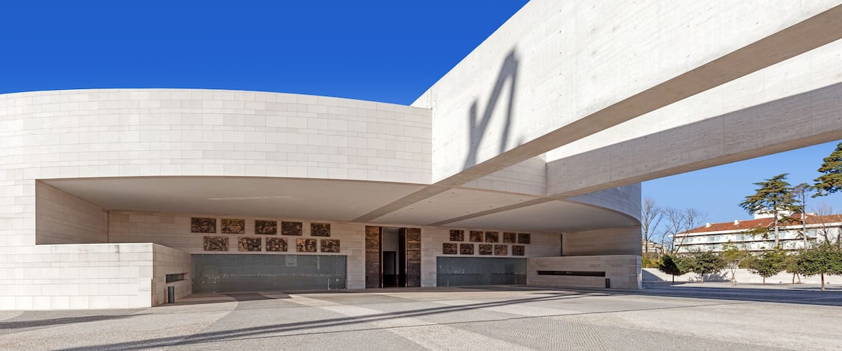 A modern architectural building with a curved facade and a series of artworks displayed on the lower wall.