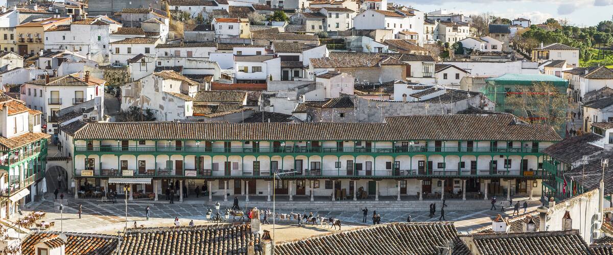 A historic town with white buildings and terracotta roofs, a central square, and a green-roofed building.