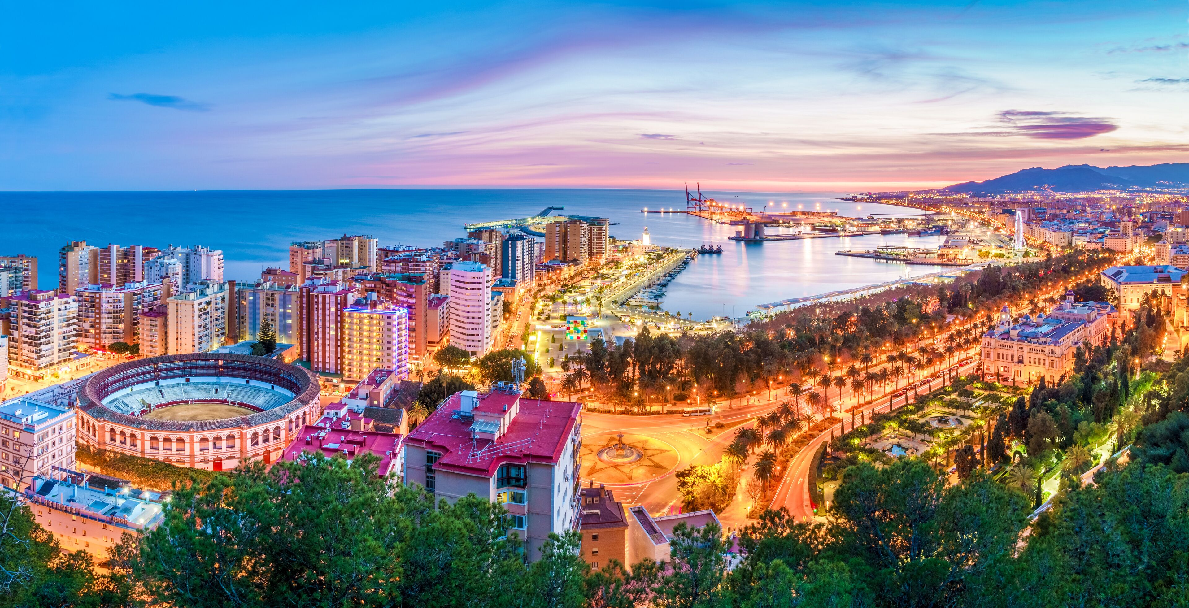 Paisagem costeira urbana com uma arena de touros em destaque, uma ponte e uma combinação de edifícios residenciais e comerciais.