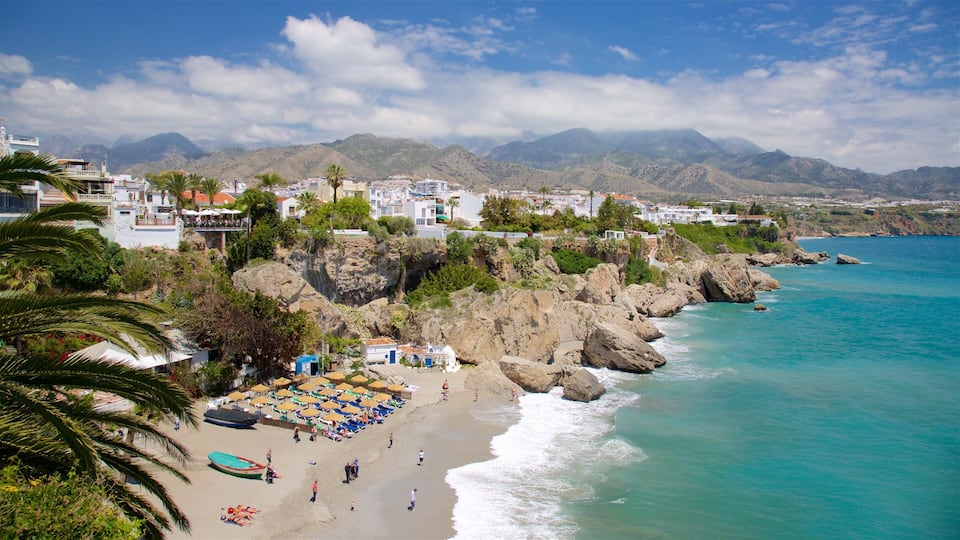 A coastal town with a beach, rocky cliffs, and mountains in the background.