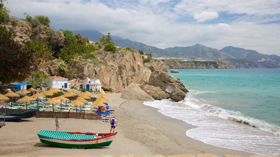 A beach with umbrellas, a boat, and a rocky cliff with houses.