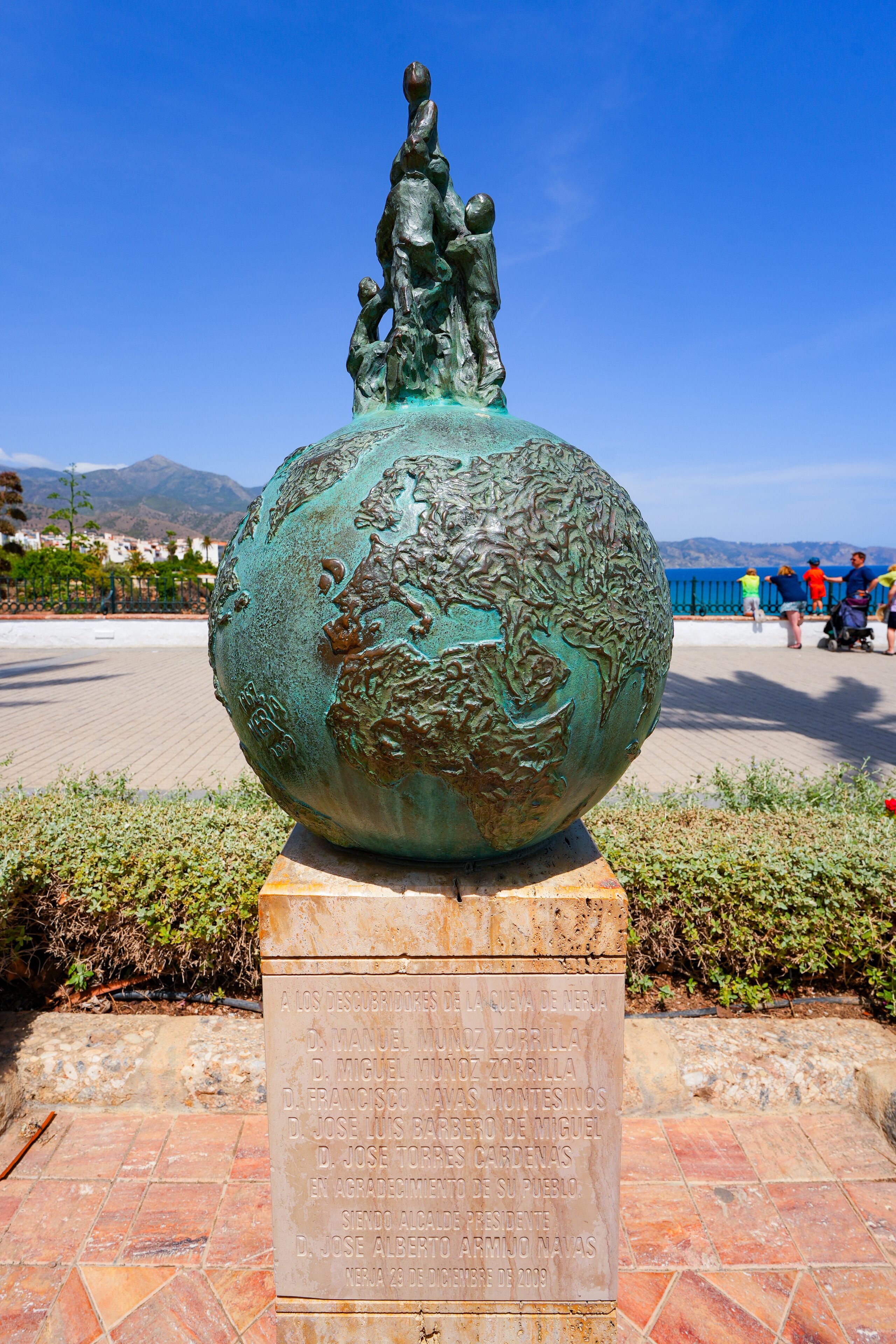 A bronze globe sculpture with inscriptions, set on a pedestal, with a clear blue sky and mountains in the background.