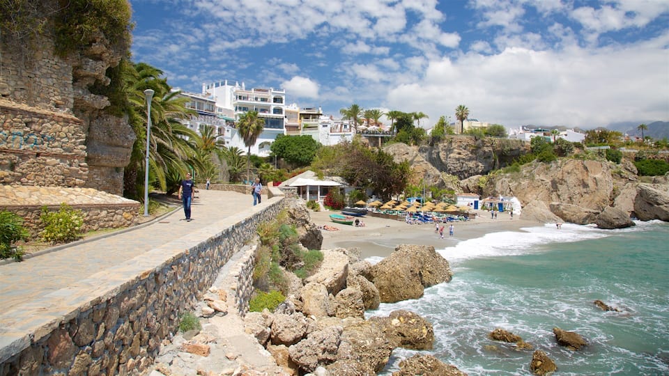 A coastal town with a stone wall, beach umbrellas, and rocky cliffs.