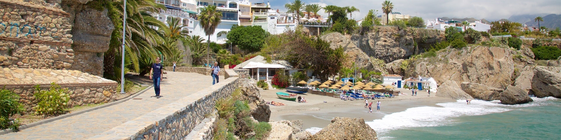 A coastal town with a stone wall, beach umbrellas, and rocky cliffs.