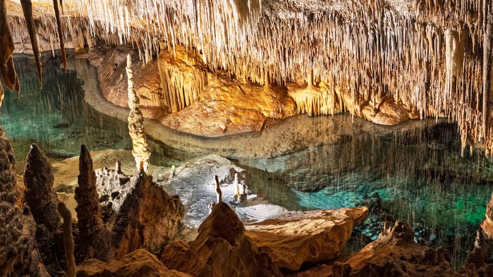 A cave with stalactites and stalagmites, a pool of water, and rock formations.