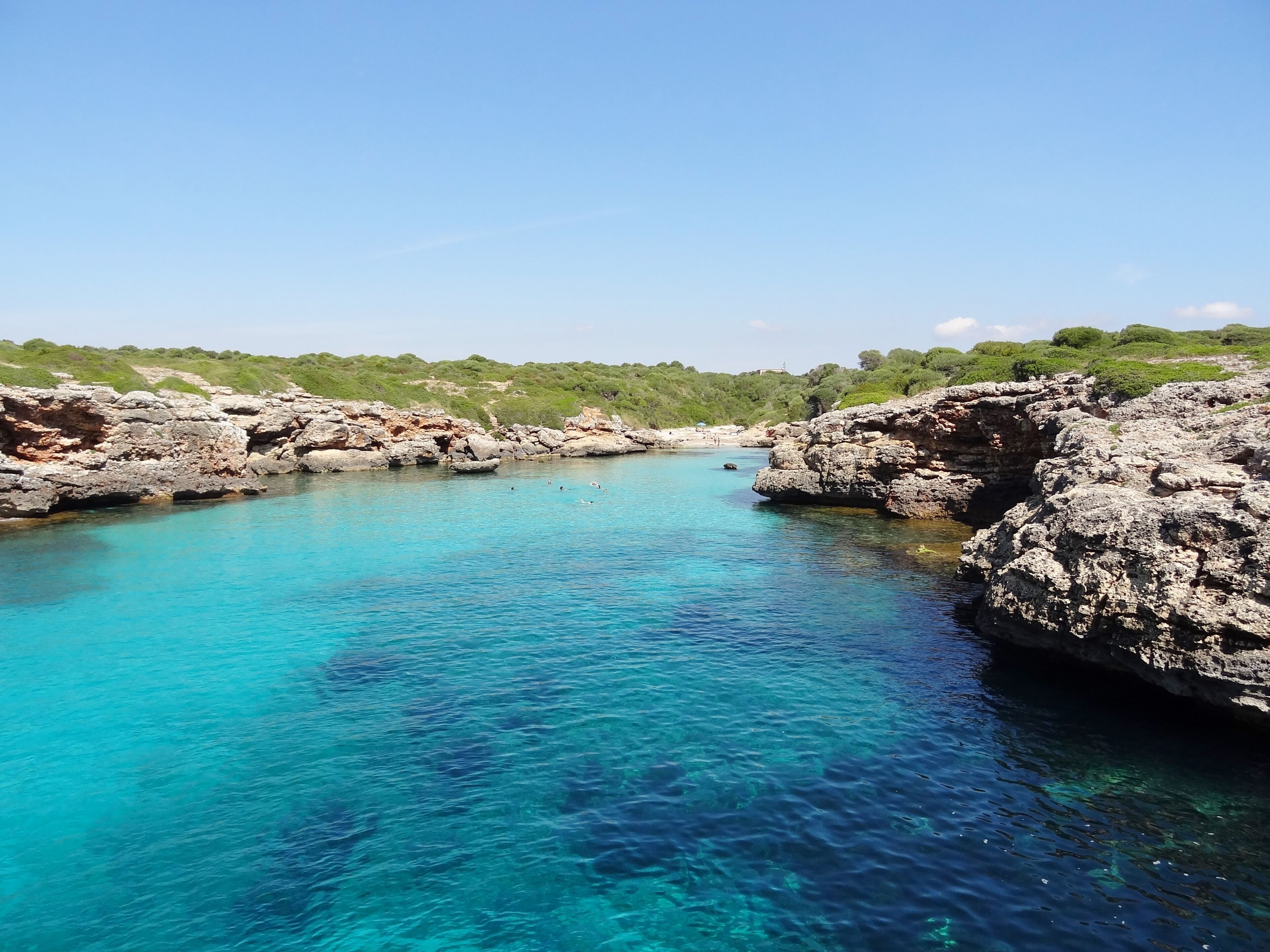 A clear blue sea surrounded by rocky cliffs and green hills.