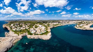 Un pueblo costero con un litoral rocoso, aguas azules cristalinas y montañas al fondo.