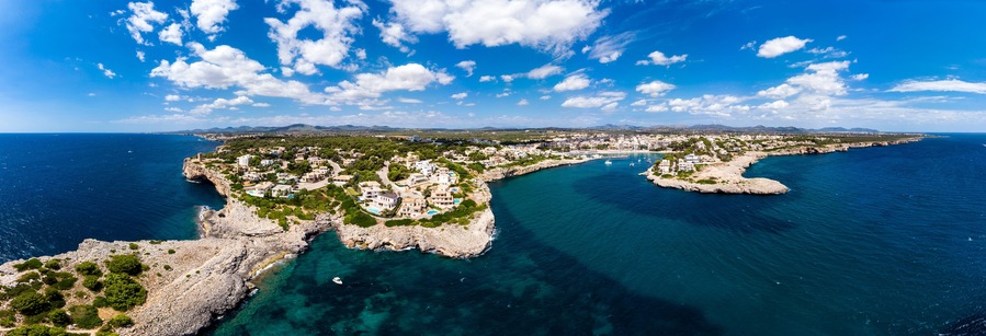 Un pueblo costero con un litoral rocoso, aguas azules cristalinas y montañas al fondo.