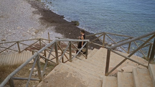 Young woman walking down wooden stairs by the rocky beach at port de valldemossa in mallorca, spain with the clear blue sea in the background