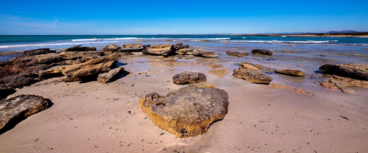 A rocky beach with large boulders and calm waves.