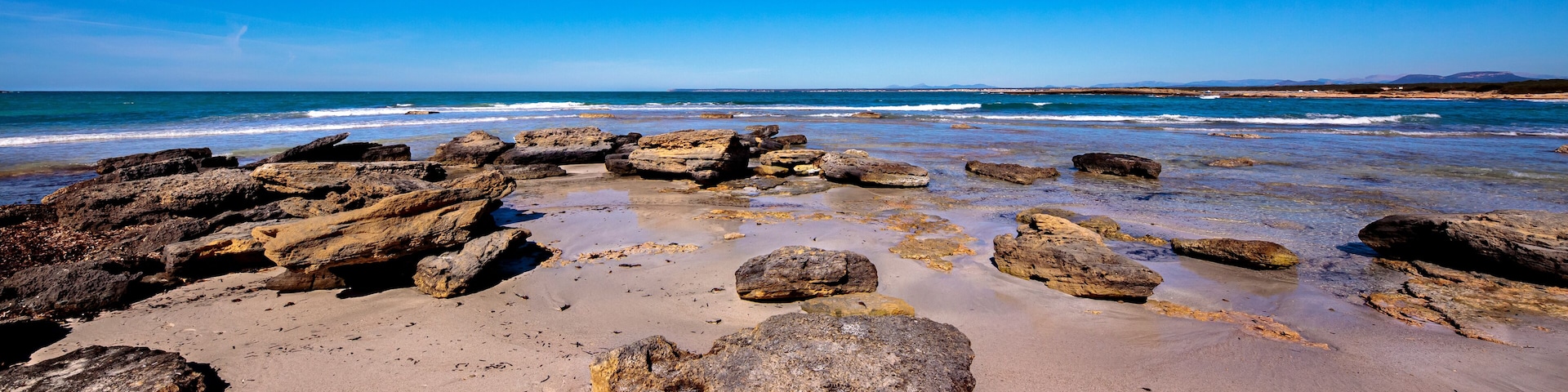 A rocky beach with large boulders and calm waves.