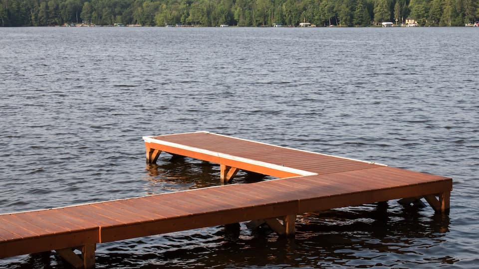 A wooden dock extending into a calm lake with a forested shoreline in the background.