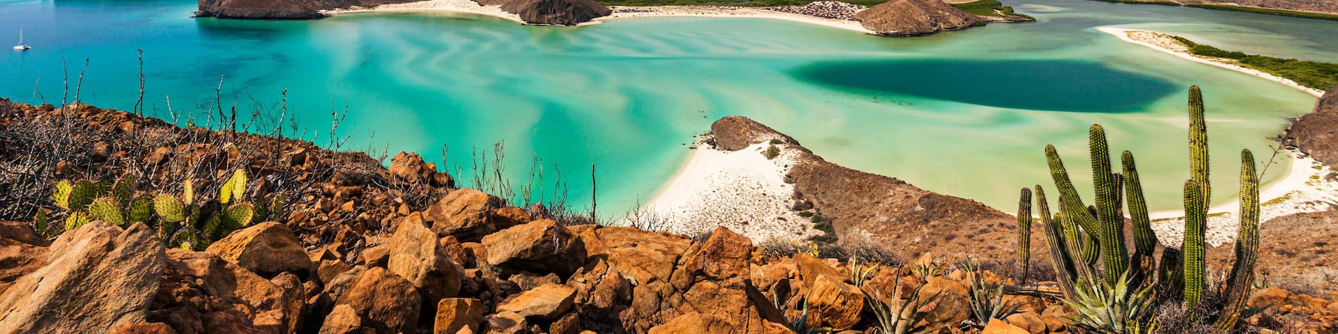 A coastal landscape with clear turquoise waters, rocky terrain, and cacti.
