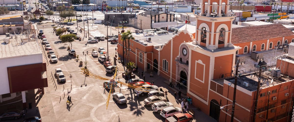 Stadsgezicht met een opvallende kerk, herkenbaar aan de koepel en de klokkentoren, omringd door palmbomen en een parkeerplaats.