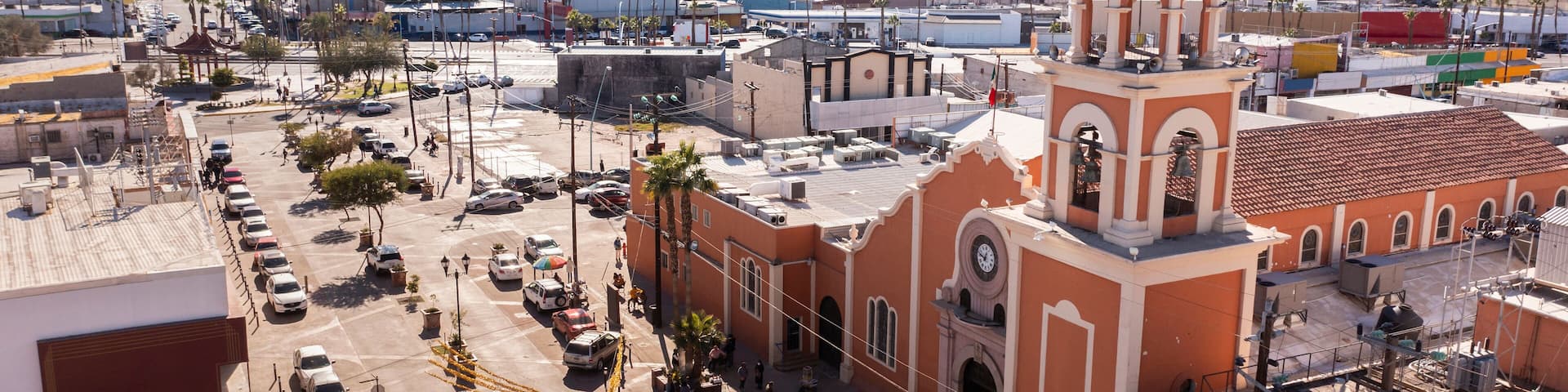 A cityscape with a prominent church featuring a dome and bell tower, surrounded by palm trees and a parking lot.